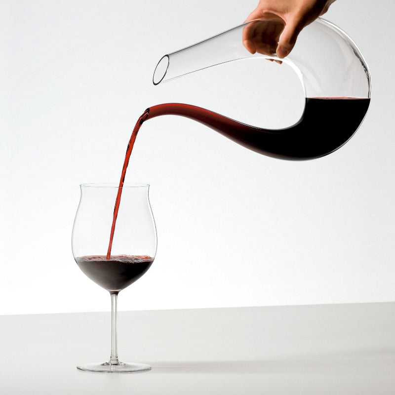 Glass wine decanter with dark amber base and clear neck, wine being poured